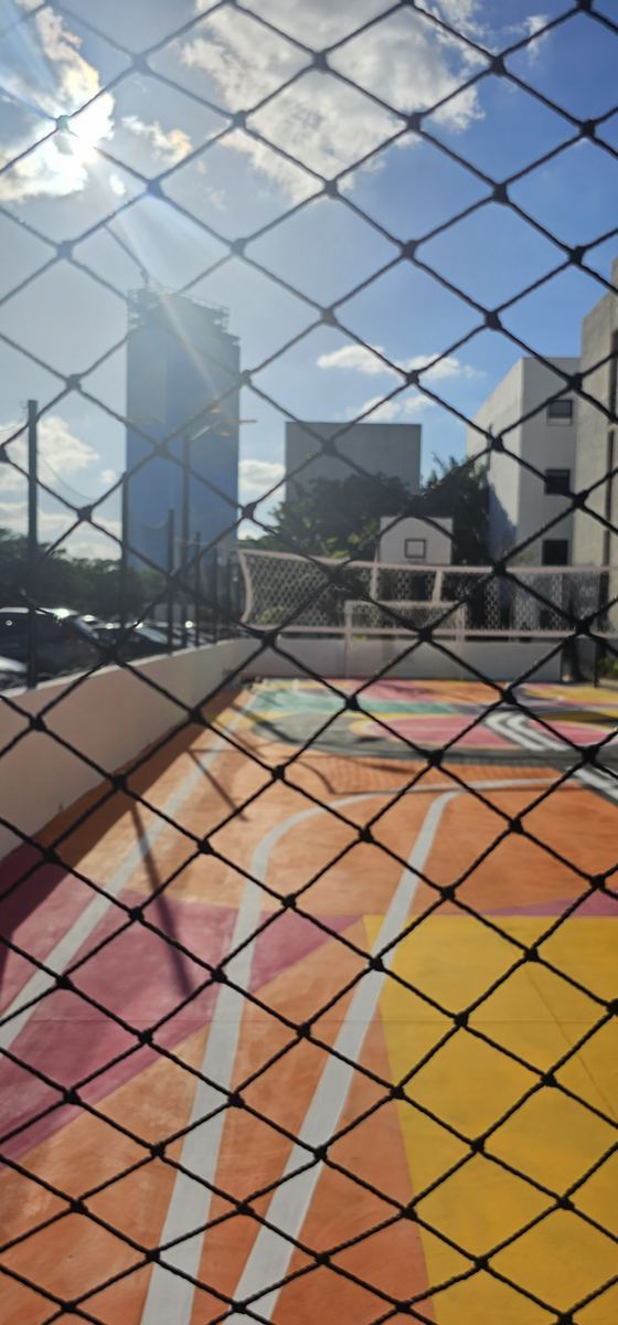 Detalle de la malla en rombo de una red perimetral negra frente a una cancha