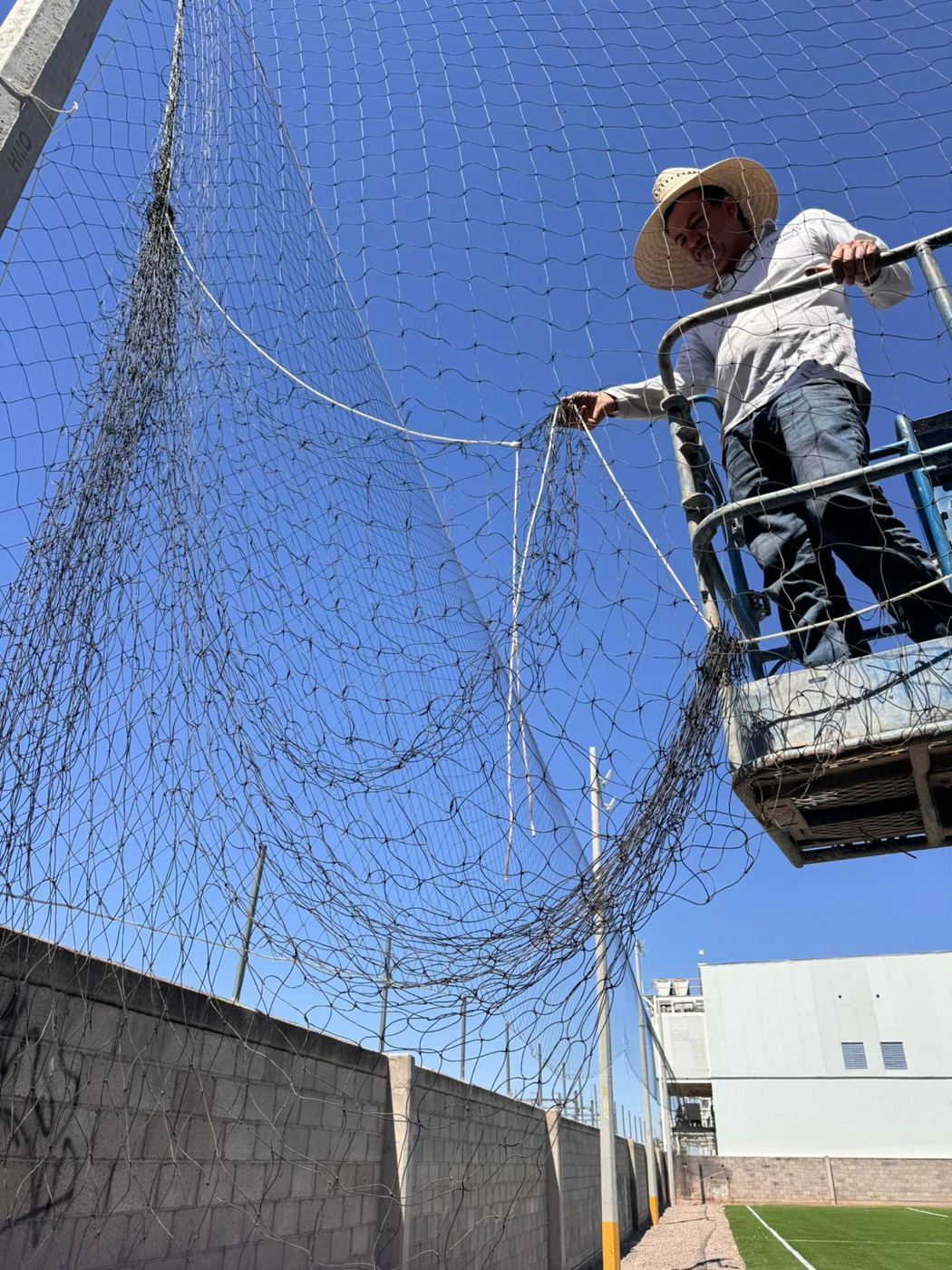 Instalador colocando red perimetral desde una canastilla elevada en una cancha de fútbol