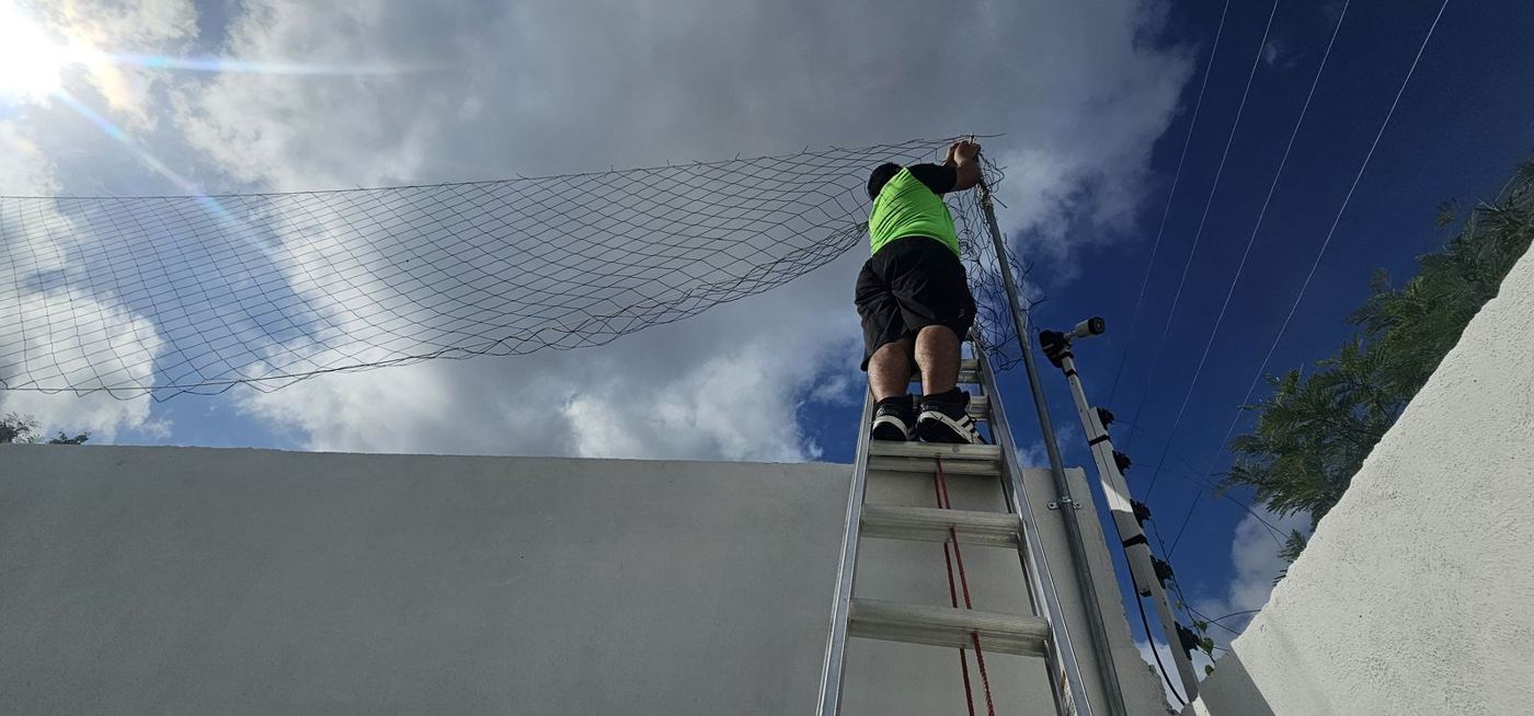 Instalador colocando una red perimetral sobre una barda desde una escalera