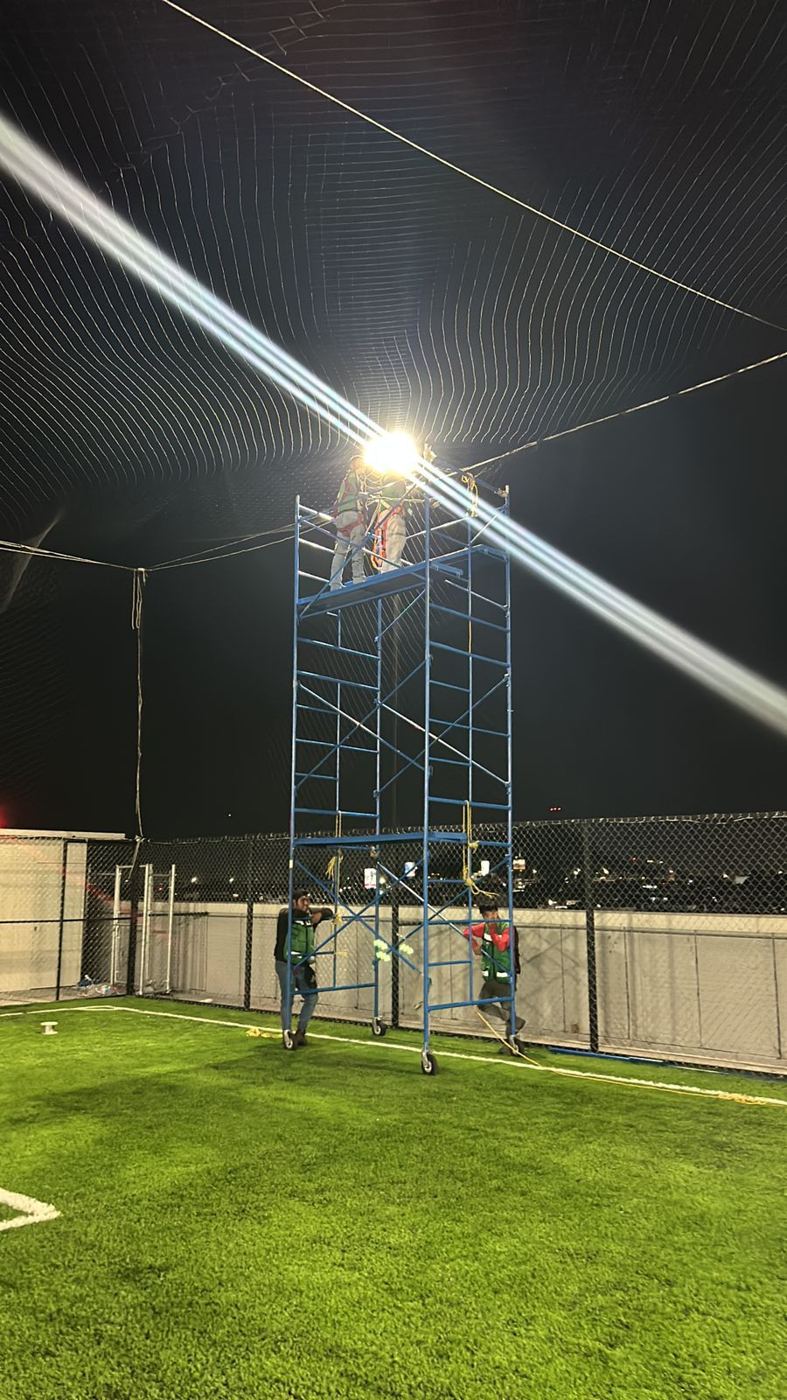 Instalación nocturna de un techo de red sobre cancha de fútbol desde andamio