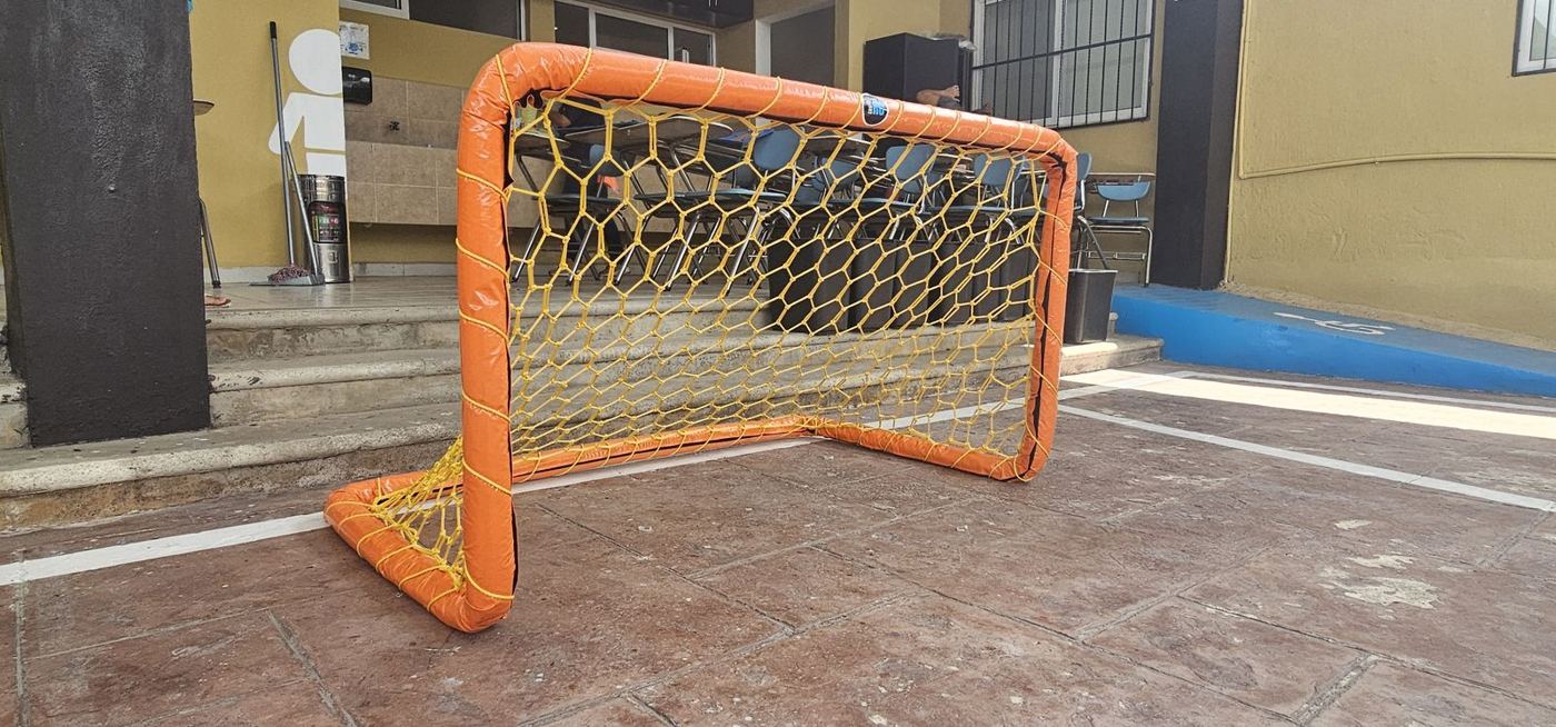 Mini portería forrada en naranja con red amarilla en el patio de una escuela