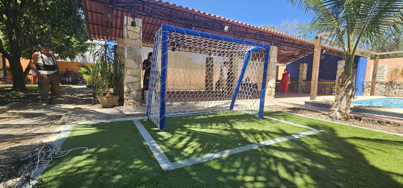 Portería de fútbol azul con red blanca en cancha de pasto sintético de una quinta