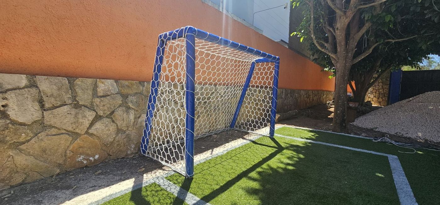 Portería de fútbol azul con red hexagonal blanca sobre pasto sintético
