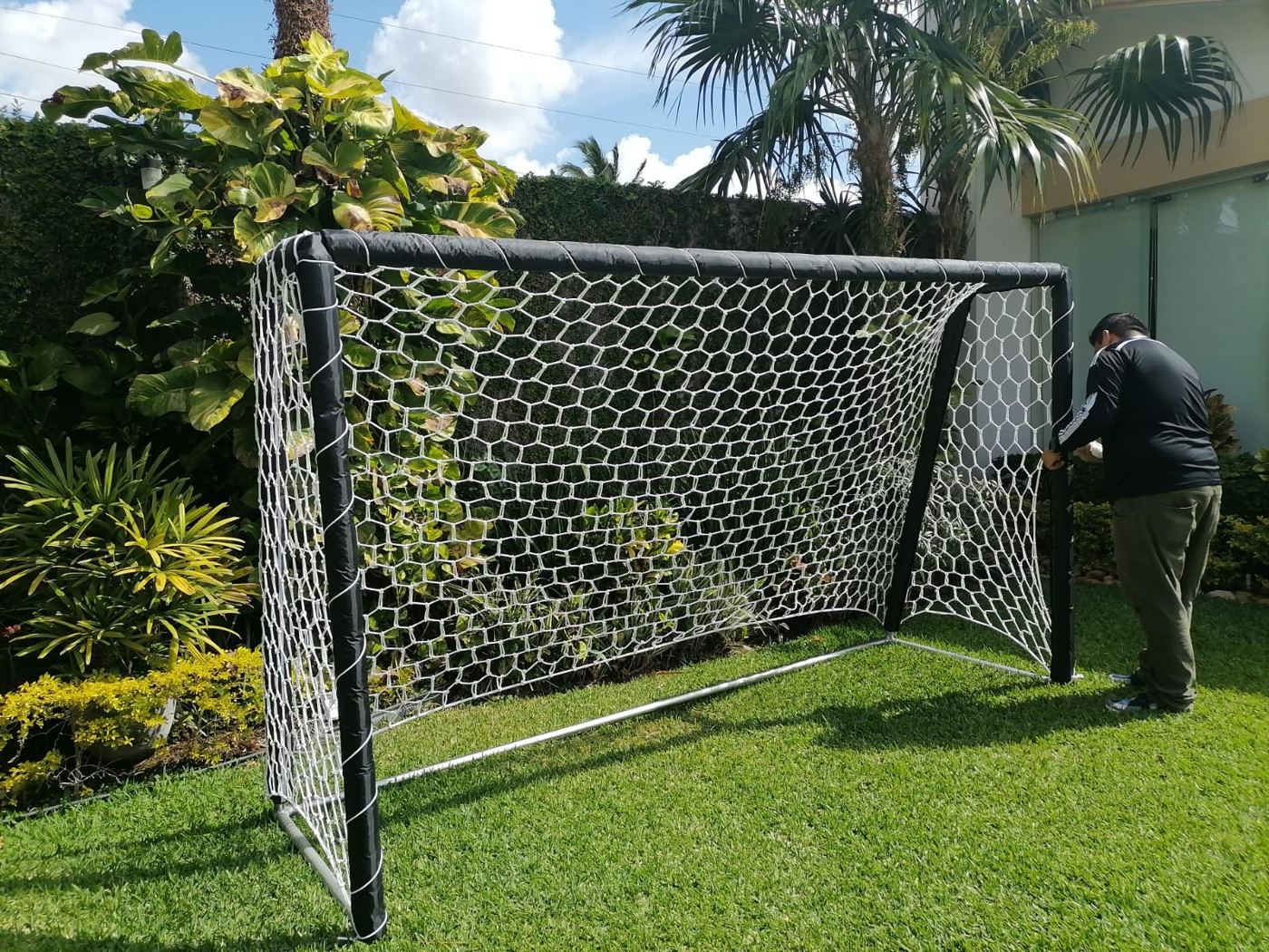 Portería de fútbol con marco negro y red hexagonal blanca en un jardín