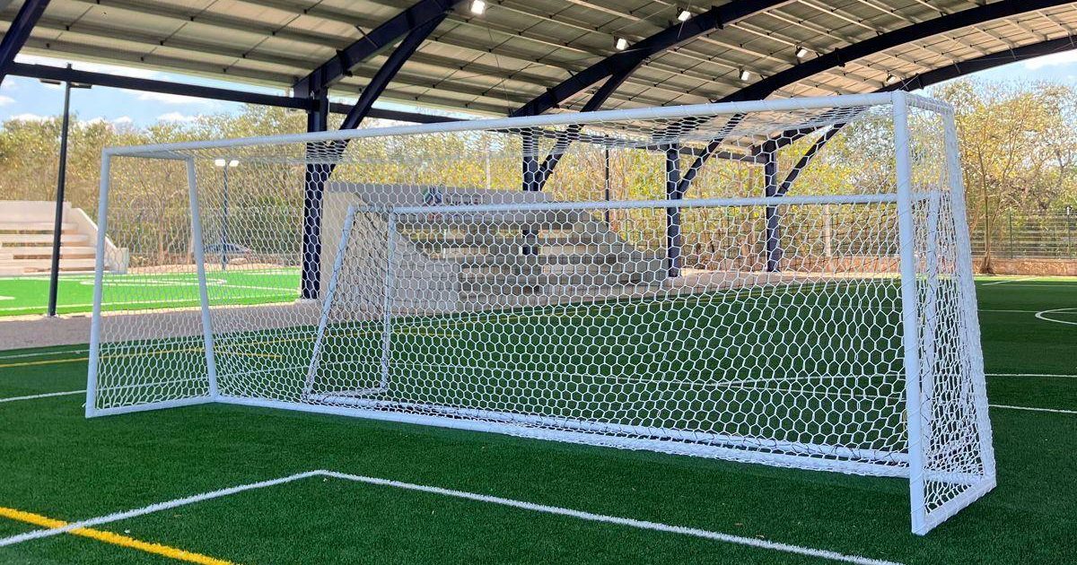 Portería de fútbol con red hexagonal blanca en una cancha de pasto sintético