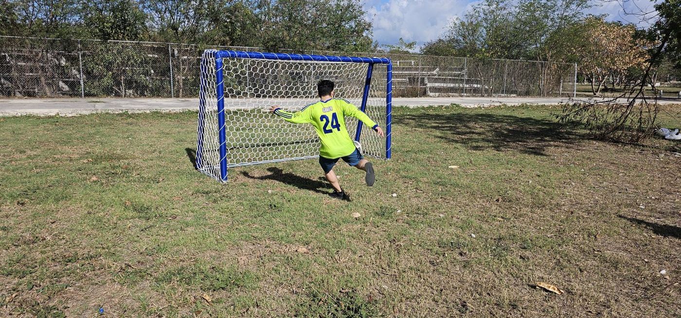 Jugador pateando hacia una portería de tubo forrado azul con red hexagonal blanca