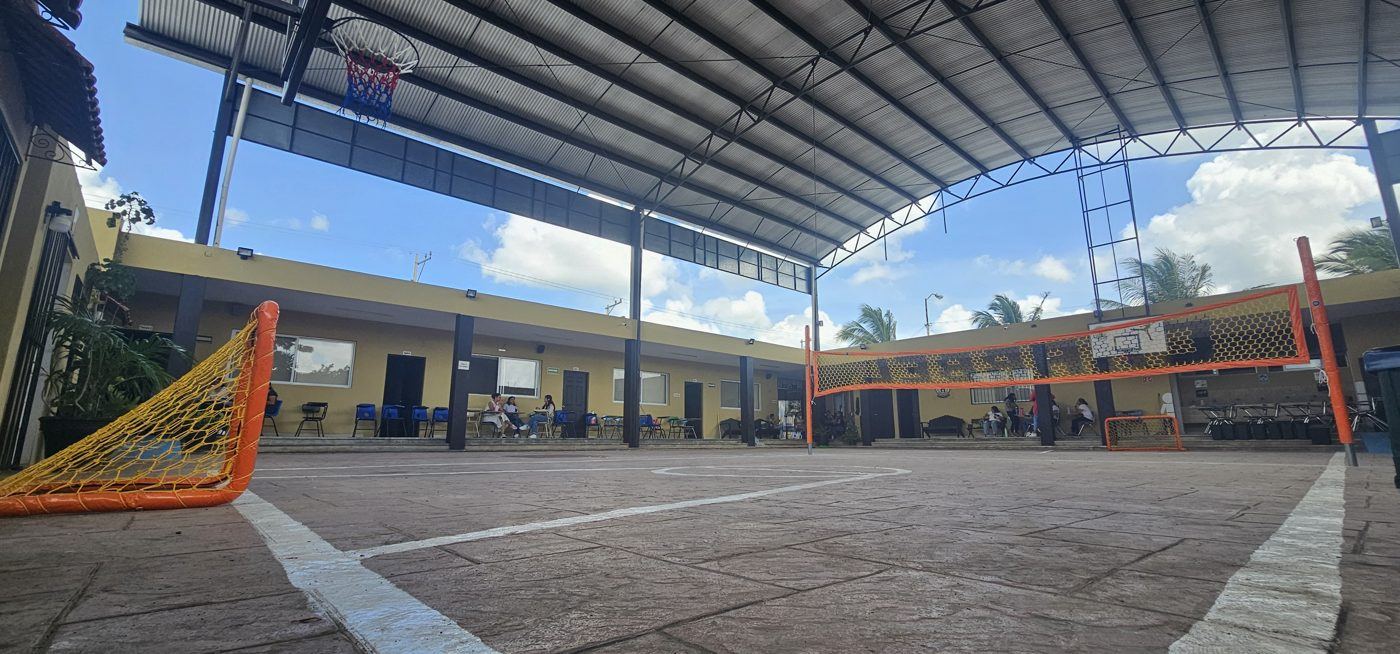 Portería infantil naranja con red amarilla en la cancha techada de un colegio