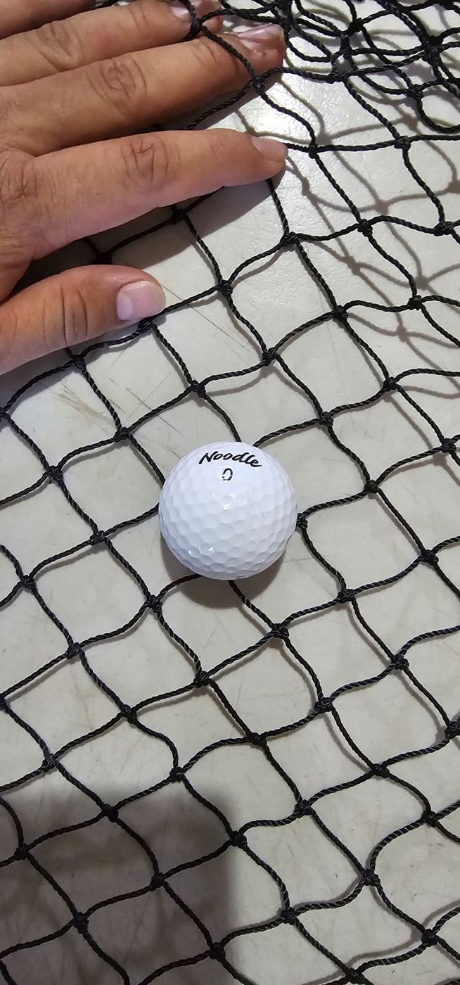 Pelota de golf sobre una red negra para comparar la abertura de la malla