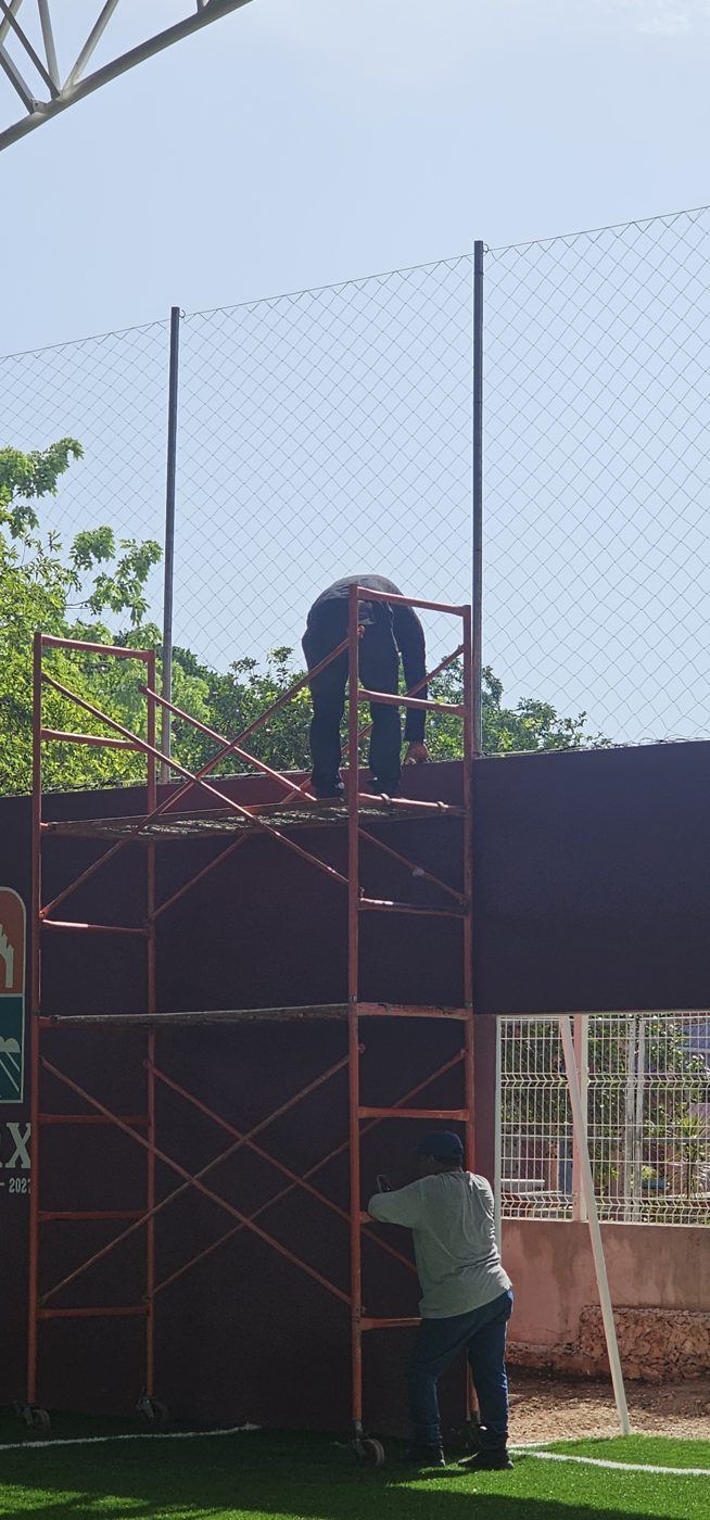 Instaladores sobre un andamio colocando una red perimetral en la cancha de una escuela
