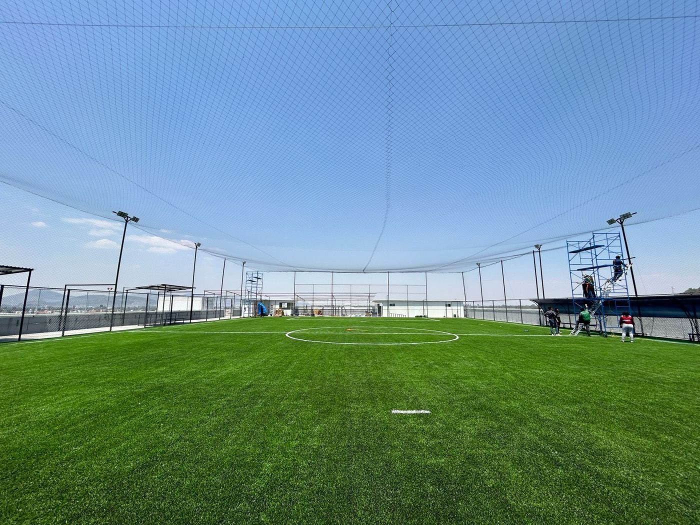 Cancha de fútbol de pasto sintético con red perimetral y techo de red